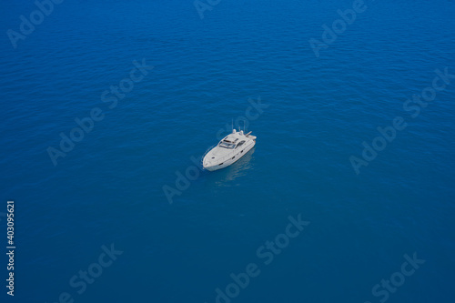 Top view of a white boat in the blue sea. Aerial view of a yacht on blue water. Lonely boat mooring on the water. luxury motor boat. Drone view of a boat. © Berg
