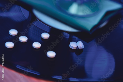 selective focus photo of pills on vinyl record background, surrounded by bright club illumination