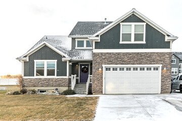 A modern dark gray and white new construction craftsman with stone accents and a purple front door in Salt Lake city on a snowy winter December day