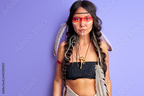 Photos woman in indian wearing and colorful makeup posing at camera, with feathers on head