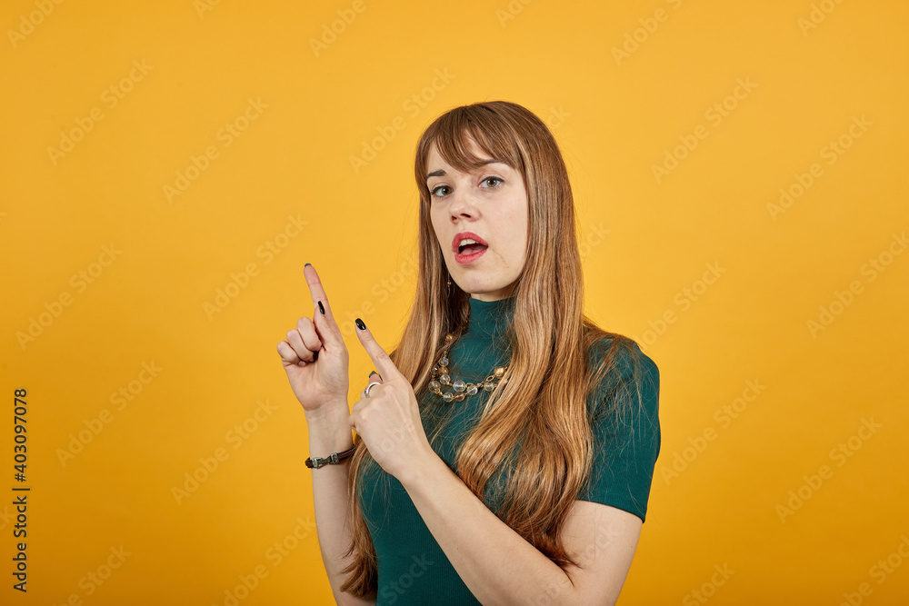 Obraz premium Hand points index finger up, pointing forefinger surprise gift option, great idea. Young attractive woman, dressed green shirt blonde hair, yellow background
