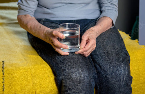 An elderly woman holds water in her hands in order to drink pills