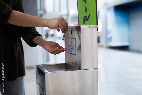 A woman wearing a surgical mask cleaning her hands at the airport during the coronavirus pandemic with a disinfectant dispenser