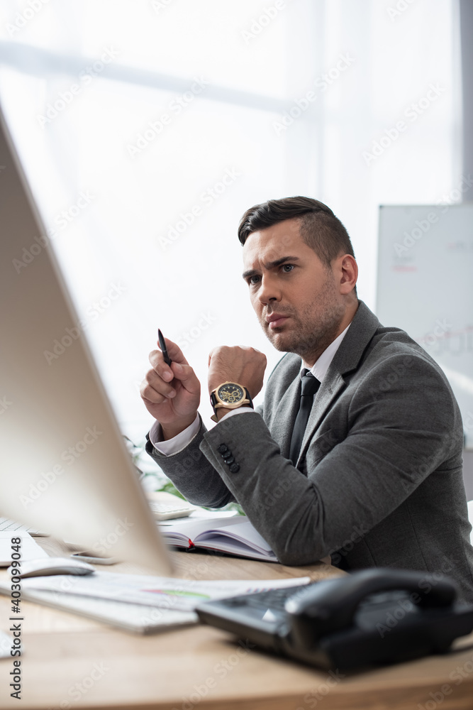 serious trader holding pen while sitting at workplace on blurred foreground serious trader holding pen while sitting at workplace on blurred foreground