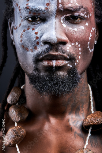 black shaman with national ethnic make-up on body, face. young male with dreadlocks is confident in himself