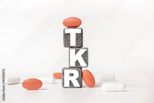 a group of white and red pills and cubes with the word TKR Total knee replacement on them, white background. Concept carehealth, treatment, therapy. photo