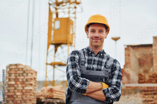 With arms crossed. Construction worker in uniform and safety equipment have job on building