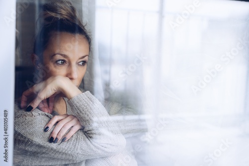 A melancholy and sad woman. Depression at home window looking depressed.