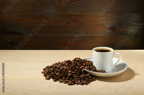 white coffee cup and coffee beans are on a wooden background. cup of aromatic coffee is on a wooden table with copy space