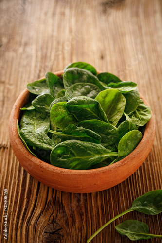 Fresh spinach leaves in a ceramic bowl on a wooden background, close up view