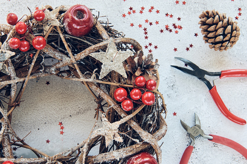 Christmas Wreath Made of branches decorated with gold wooden stars and red berry bubbles. Creative diy craft hobby. Making handmade christmas decorations. Top view class with metal pliers, nippers