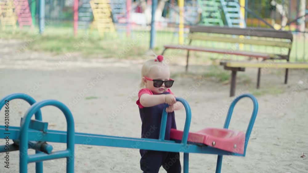A little girl in sunglasses on the playground rocks the swing herself. A little girl in sunglasses on the playground rocks the swing herself.