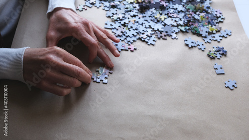 woman in white sweater doing puzzle.Female's hands and puzzle pieces on the table.
