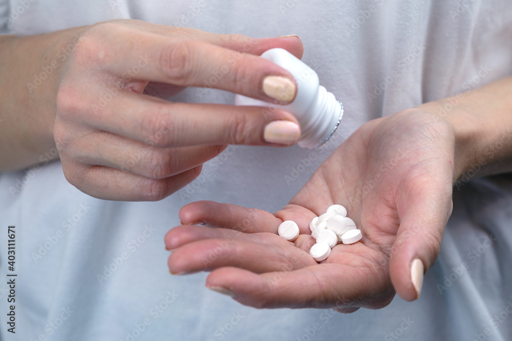 Woman pours pills from a white bottle in her hand. Woman pours pills from a white bottle in her hand.