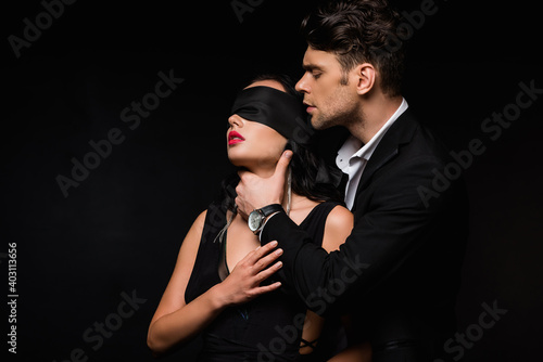 Fotografía man in suit choking blindfolded woman in dress isolated on black