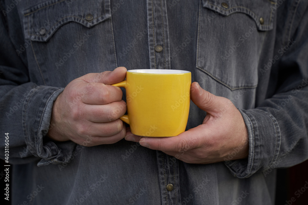 Man holding big yellow mug in his hands wearing grey jeans shirt. Slowing down concept. High quality photo Man holding big yellow mug in his hands wearing grey jeans shirt. Slowing down concept. High quality photo