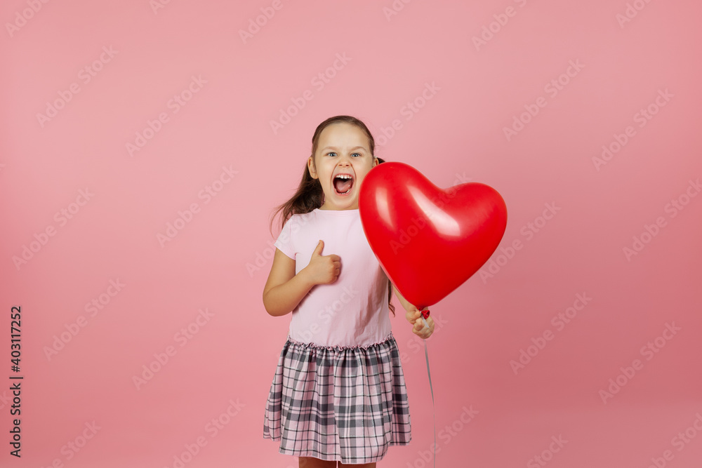 close-up enthusiastic, ecstatic, rapturous girl in pink dress holds a red balloon in the shape of a heart and gives a thumbs up isolated on a pink background. close-up enthusiastic, ecstatic, rapturous girl in pink dress holds a red balloon in the shape of a heart and gives a thumbs up isolated on a pink background.