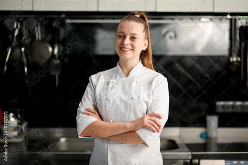 young beautiful smiling woman chef with arms crossed at kitchen