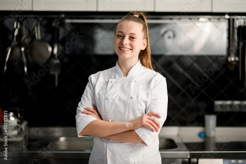 young beautiful smiling woman chef with arms crossed at kitchen photo