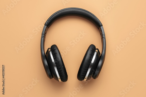 Close-up photo of stylish modern black chrome headphones over beige background.