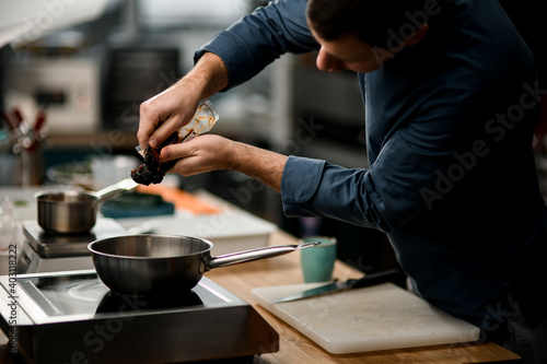 man chef holds package with product and puts it on frying pan