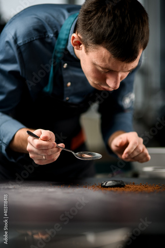 male chef holds steel spoon in his hand and carefully lays the ingredients