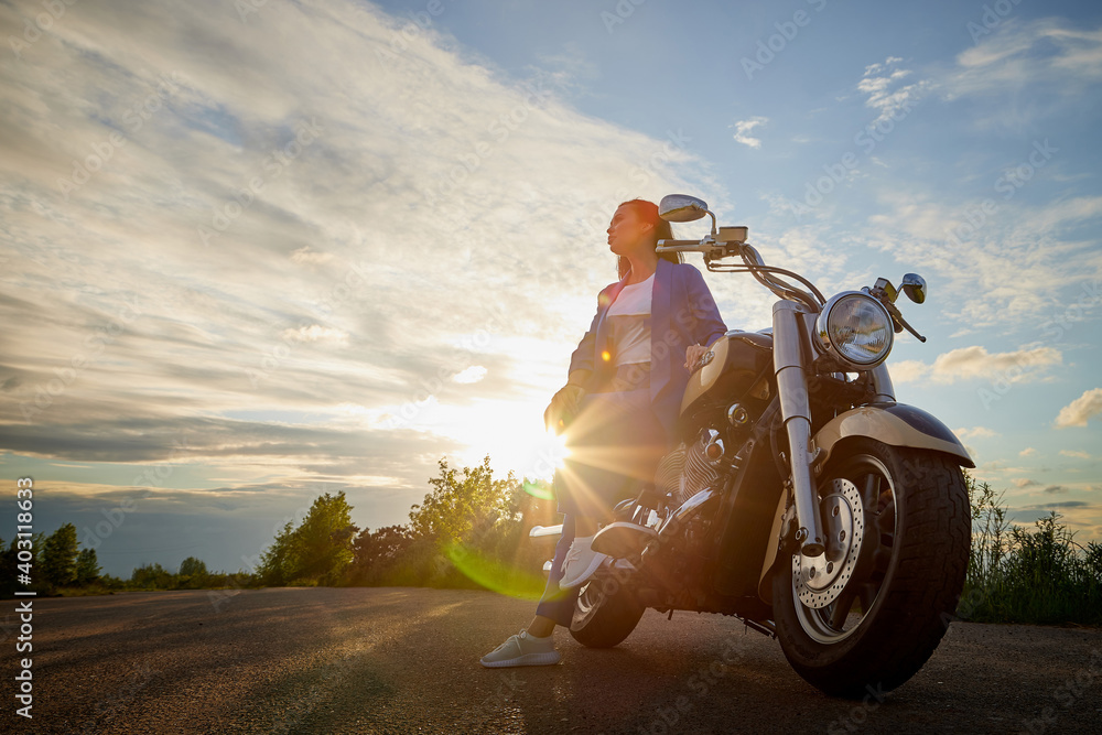 Fototapeta premium Attractive brunette motorcyclist with motorcycle in a summer evening during sunset. Adventure and travel concept.