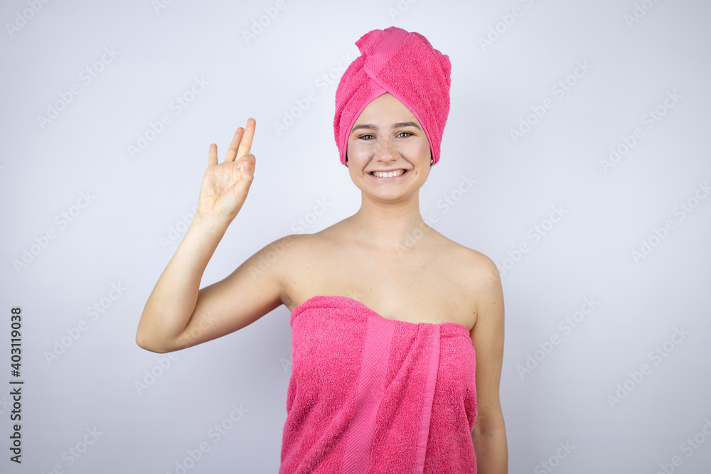 Young beautiful woman wearing shower towel after bath standing over isolated white background doing ok sign with fingers and smiling, excellent symbol Young beautiful woman wearing shower towel after bath standing over isolated white background doing ok sign with fingers and smiling, excellent symbol