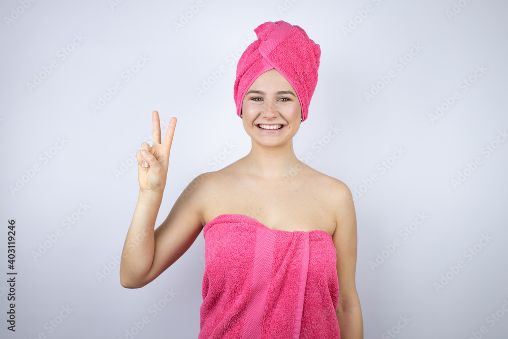 Young beautiful woman wearing shower towel after bath standing over isolated white background showing and pointing up with fingers number two while smiling confident and happy Young beautiful woman wearing shower towel after bath standing over isolated white background showing and pointing up with fingers number two while smiling confident and happy