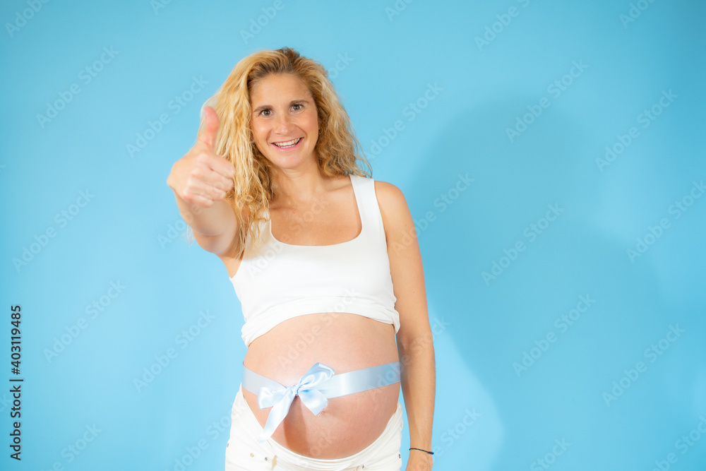 Fototapeta premium Smiling pregnant woman with thumb up and wearing a blue laze around the belly.