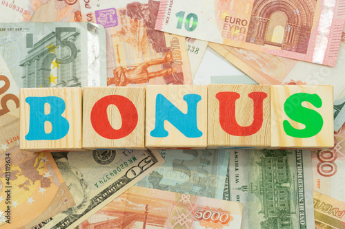 The inscription bonus in multicolored cubes on the background of banknotes euro dollars rubles