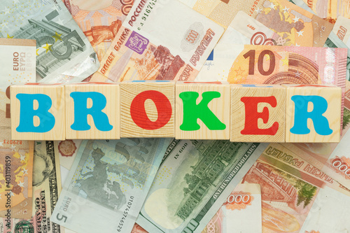 The inscription broker in multicolored cubes on the background of banknotes euro dollars rubles