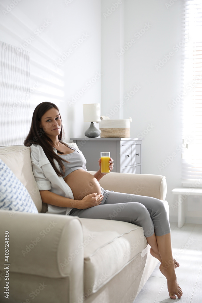 Young pregnant woman with glass of juice in living room. Taking care of baby health Young pregnant woman with glass of juice in living room. Taking care of baby health