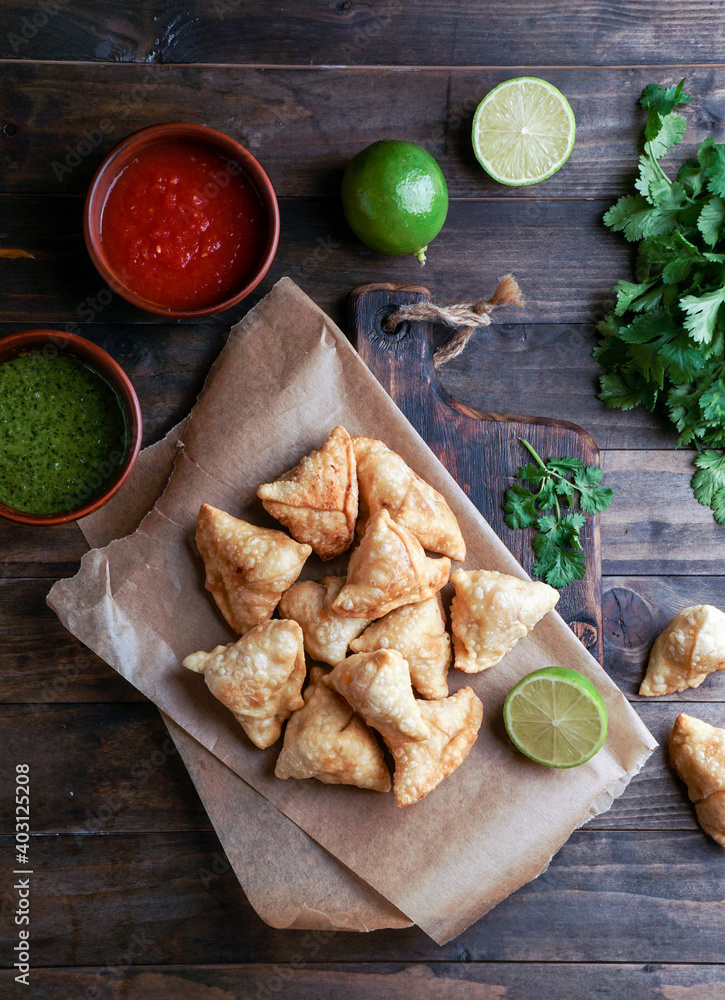 Samosa - fried/baked pastry with filling, popular Indian snacks, served in bowl with spices and fresh cilantro on rustic background Samosa - fried/baked pastry with filling, popular Indian snacks, served in bowl with spices and fresh cilantro on rustic background