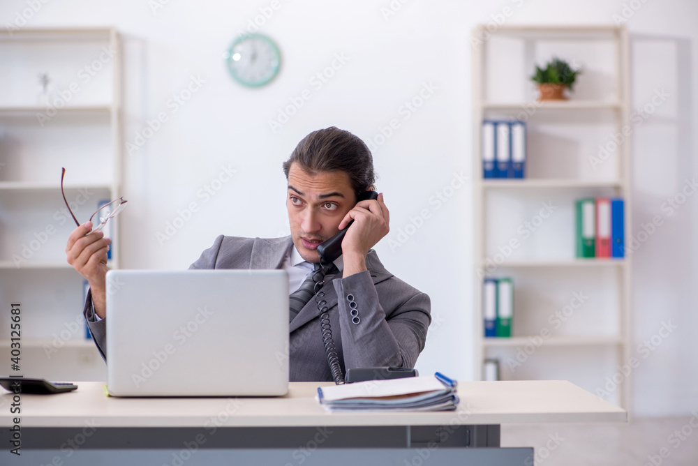 Young male employee talking by phone in the office Young male employee talking by phone in the office