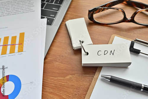 There is a piece of paper with a graph printed on it  a clipboard  and an open vocabulary book on the desk. The word CDN is there. It s an acronym that means Content Delivery Network.