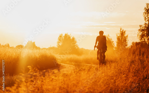 Cyclist on a gravel bike riding on a dusty trail in a field at sunset. Selective focus. © Артур Ничипоренко