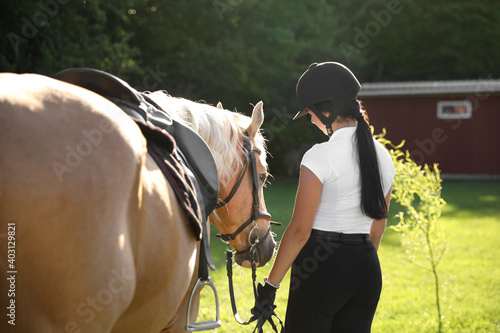 Young woman in horse riding suit and her beautiful pet outdoors on sunny day, back view