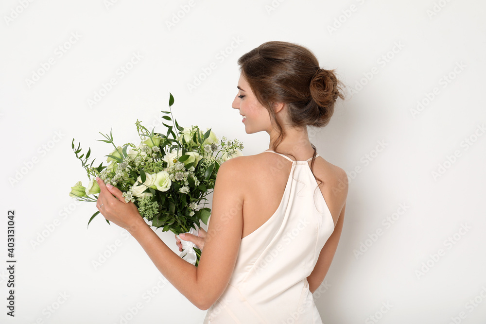 Young bride wearing wedding dress with beautiful bouquet on light background Young bride wearing wedding dress with beautiful bouquet on light background
