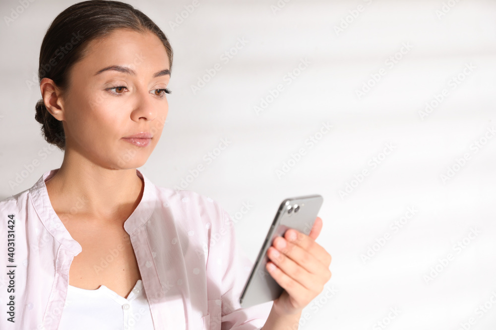 Young woman unlocking smartphone with facial scanner near white wall, space for text. Biometric verification Young woman unlocking smartphone with facial scanner near white wall, space for text. Biometric verification