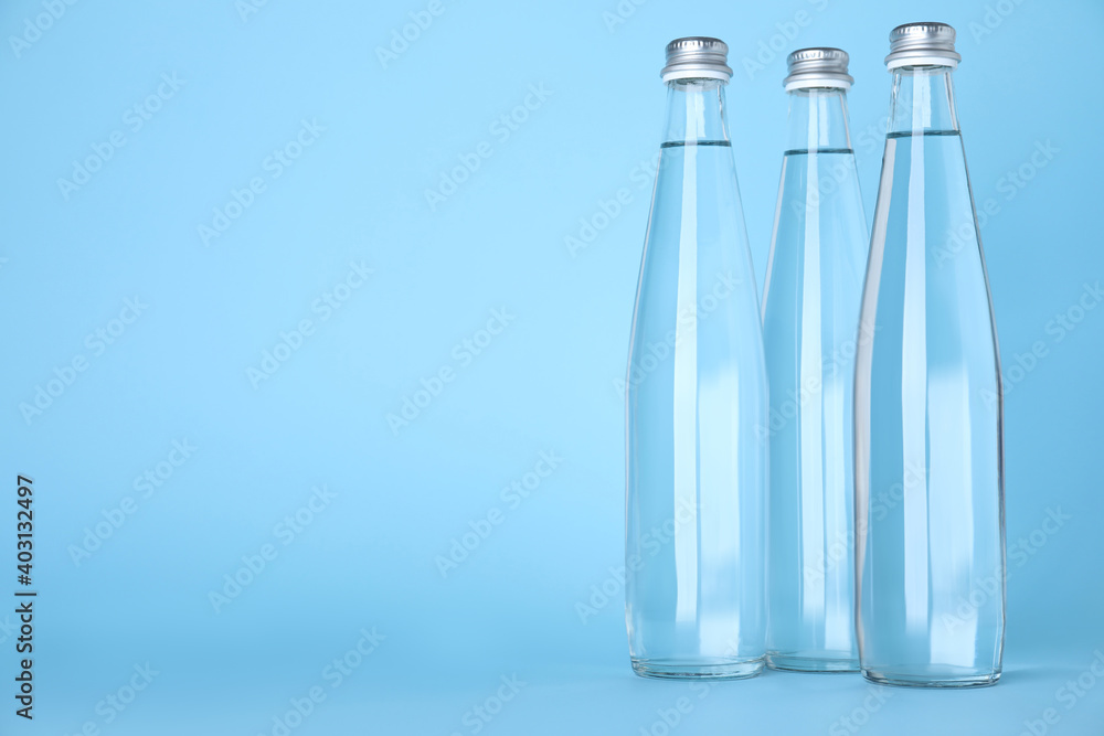 Glass bottles with water on light blue background, space for text - obrazy, fototapety, plakaty 