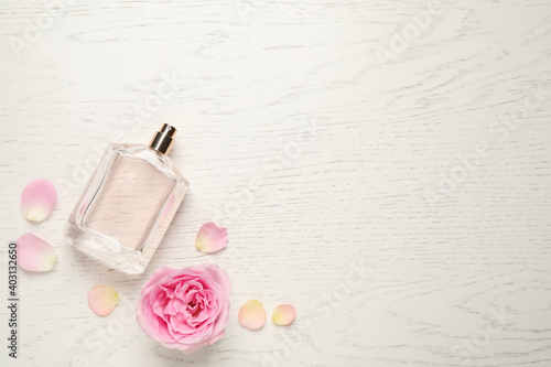 Flat lay composition with bottle of perfume and rose on white wooden background  space for text