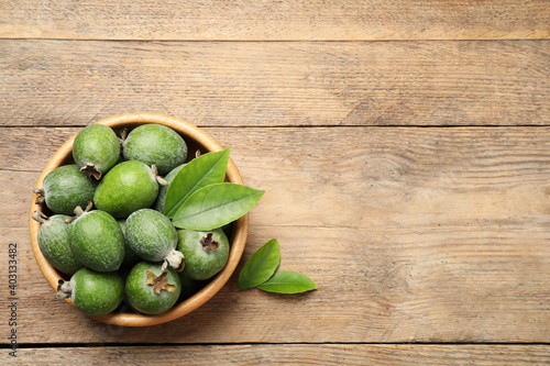 Top view of fresh green feijoa fruits in bowl on wooden table, space for text