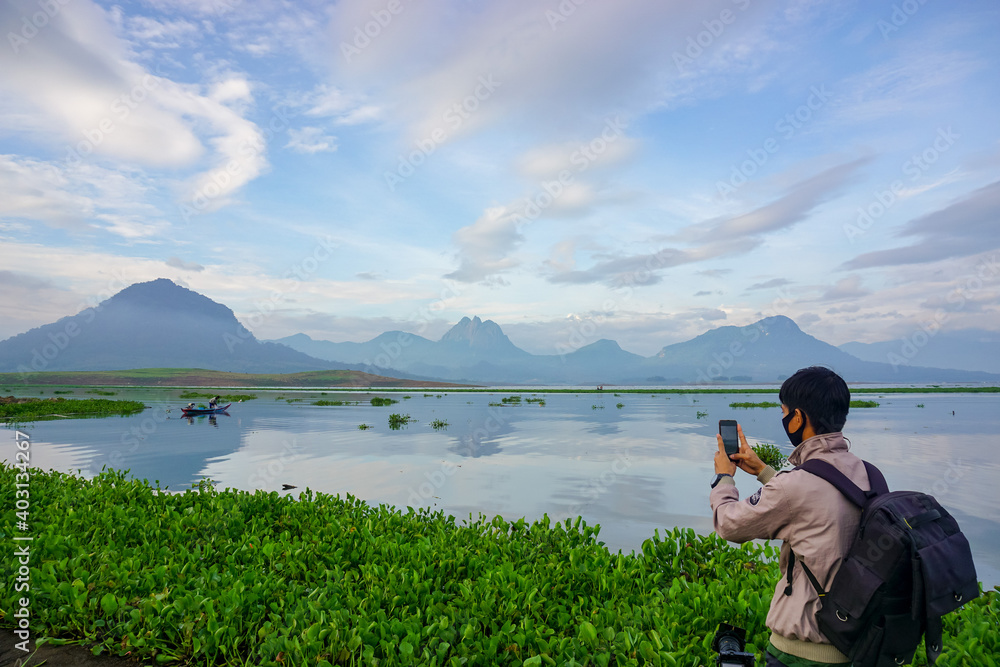A young man is taking pictures on the lake using smartphone. For traveler or youtuber content. 