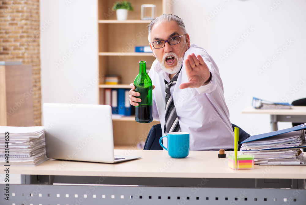 Old male employee drinking alcohol in the office Old male employee drinking alcohol in the office