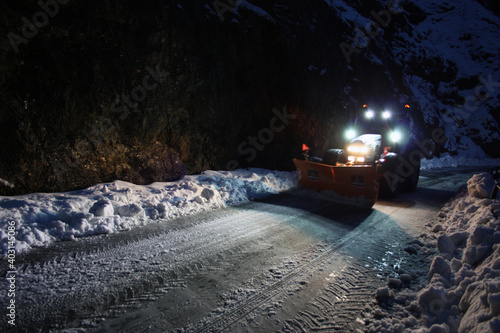 snowplow passes through the snowy mountain streets in the evening to clean up the road traffic