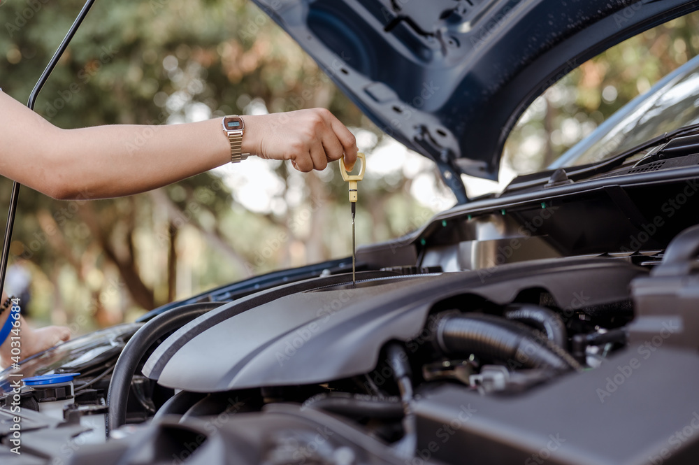 A woman self service use dipstick checking engine oil level car vehicle,professional maintenance and repair before travel transportation for safety driving on street road.Holiday,travel and vacation A woman self service use dipstick checking engine oil level car vehicle,professional maintenance and repair before travel transportation for safety driving on street road.Holiday,travel and vacation