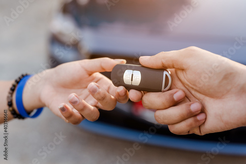 Close up woman holding new car systems key of blue hatchback car after buying from dealer at outdoor.