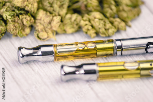 THC/CBD cannabis vape pens up-close with marijuana leaf on white wooden table