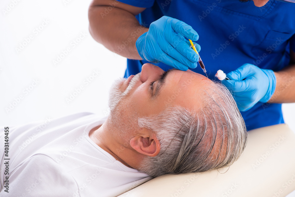 Old man visiting young male doctor in hair transplantation conce Old man visiting young male doctor in hair transplantation conce